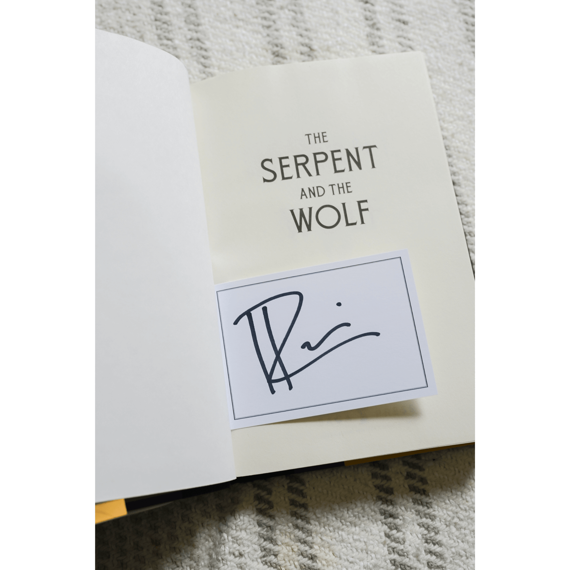 Inside a book titled 'The Serpent and the Wolf' with an author's signature card.
