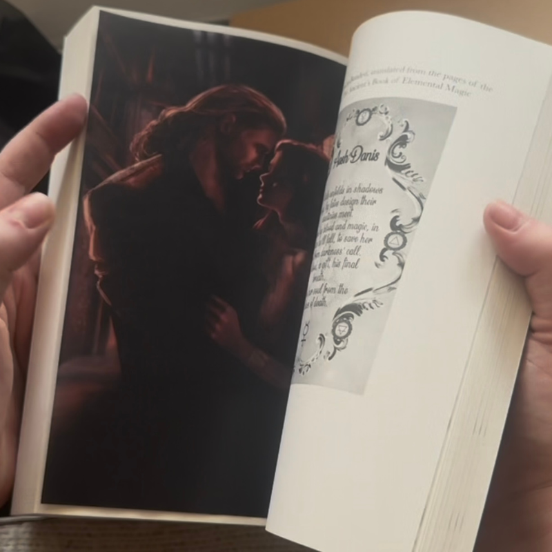 Close-up of A Dream of Blood and Magic by Olivia Boothe opened to reveal the exclusive vellum art insert, showing two characters in a romantic embrace printed on translucent overlay pages.